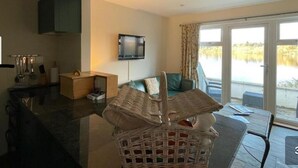 A modern living room with a large window, a flat-screen TV mounted on the wall, and a dining area with a table and chairs. - Portsonachan Hotel (Dalmally)