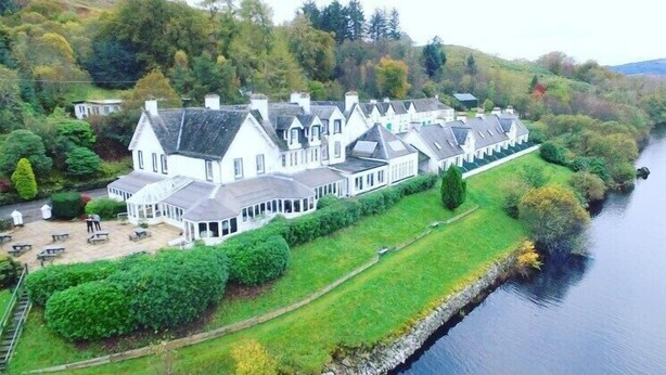 A large, white, multi-story building with a symmetrical roofline, located beside a calm river. - Portsonachan Hotel (Dalmally)