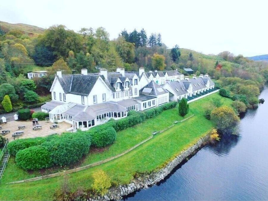 A large, white, multi-story building with a symmetrical roofline, located beside a calm river.