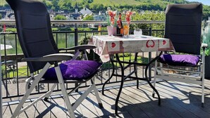 Eine Terrasse mit zwei Stühlen, einem Tisch mit floralem Tischläufer und einem schönen Blick auf Hügel und Gebäude.