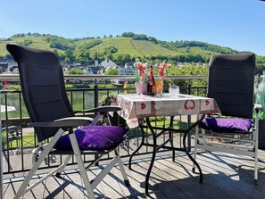 A terrace with two chairs, a table with a floral tablecloth, and a scenic view of hills and buildings. - Helene vacation apartment with balcony and Moselle view at Ferienhaus Moselwelt (Zell (Mosel))