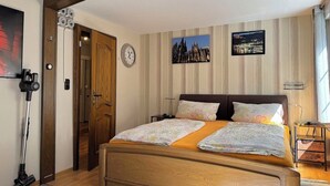 Ein Schlafzimmer mit einem hölzernen Bett, einer Uhr, zwei gerahmten Bildern und einem Staubsauger.