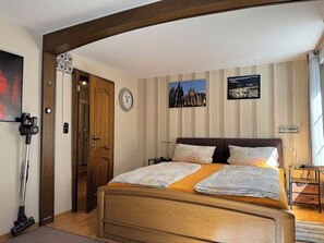 Ein Schlafzimmer mit einem hölzernen Bett, einer Uhr, zwei gerahmten Bildern und einem Staubsauger.