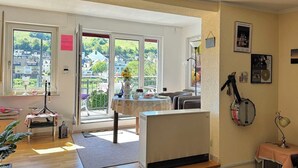 Ein Zimmer mit Heizkörper, einem Tisch mit einer Vase, einer Banjo und einem Fenster mit Blick auf Häuser.