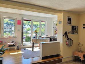 A room with a radiator, a table with a vase, a banjo, and a window with a view of houses. - Helene vacation apartment with balcony and Moselle view at Ferienhaus Moselwelt (Zell (Mosel))