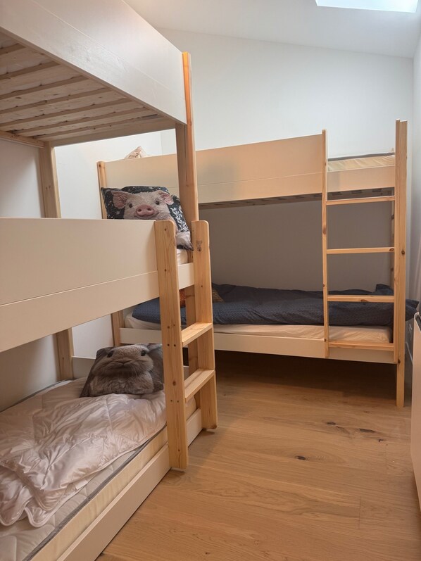 A bunk bed room with a skylight, wooden flooring, and a small ladder.