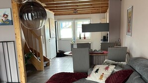 A modern living room with a grey sofa, a wooden coffee table, and a red throw blanket. There is a staircase leading to another level, and a kitchen area is visible in the background. - Vacation home "Leuchtturmblick" in the harbor village Rheinsberg (Rheinsberg)