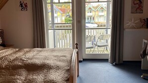 A bedroom with a wooden ceiling, a bed, a balcony with a view of houses, and a chair outside. - Vacation home "Leuchtturmblick" in the harbor village Rheinsberg (Rheinsberg)