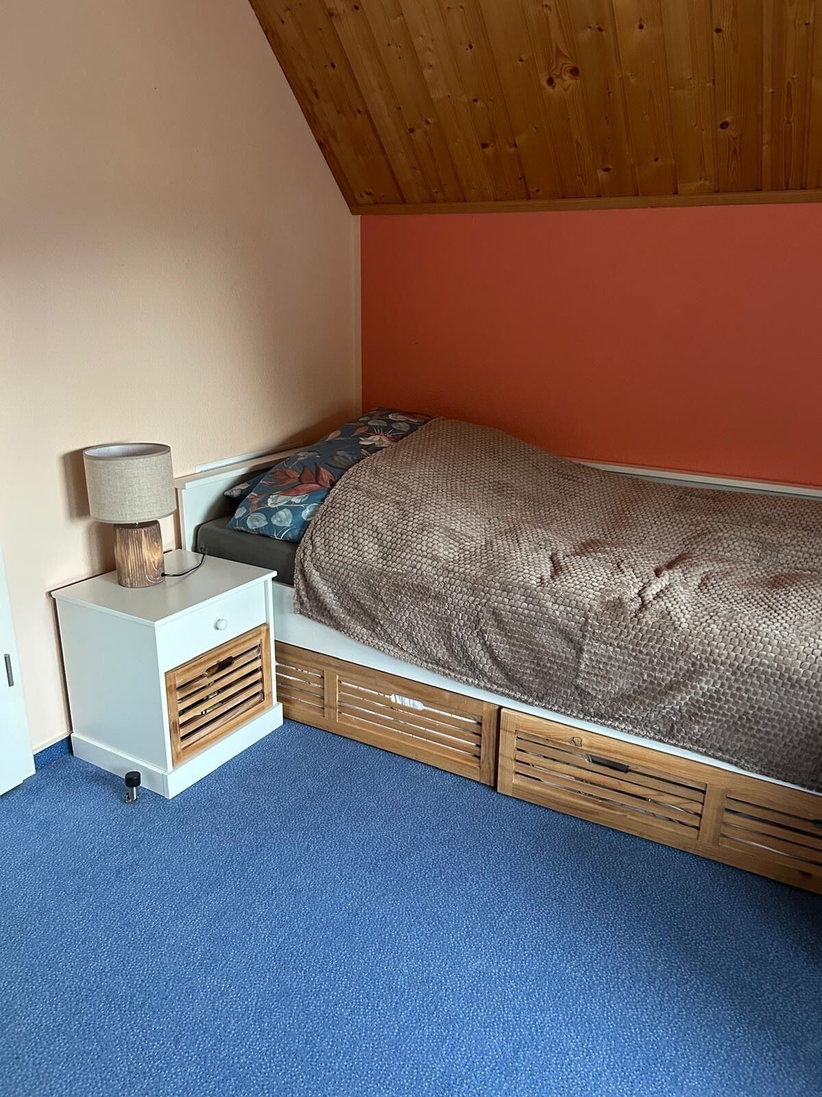 A bedroom with a bed, a nightstand, a lamp, and a blue carpet.