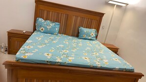 Ein Bett mit floralem Überwurf und passenden Kissen, ein Holz-Kopfteil und Nachttische, auf einem Tisch eine Fernbedienung.