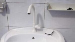 Ein weißes Waschtuch mit Wasserhahn, einer Seifenspender und einem kleinen Regal darüber.