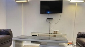 Ein modernes Wohnzimmer mit einem Wand-Fernseher, einem weißen Couchtisch mit Glasplatte und zwei braunen Ledersofas.