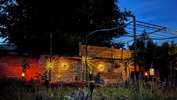 A rustic outdoor area with a stone wall, wooden bench, and decorative lighting.