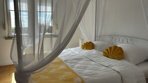 A bedroom with a canopy bed, white bedding, and a yellow patterned throw.