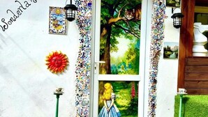 A dog sitting on a green mat in front of a door with a mosaic border, a painting of a girl in a blue dress, and the word "Wonderland" on the wall. - Wonderland21 (Saint-Germain-sur-Morin)