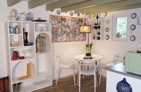 A dining area with white chairs, a round table, and a wall decorated with various plates and a collage of cards.