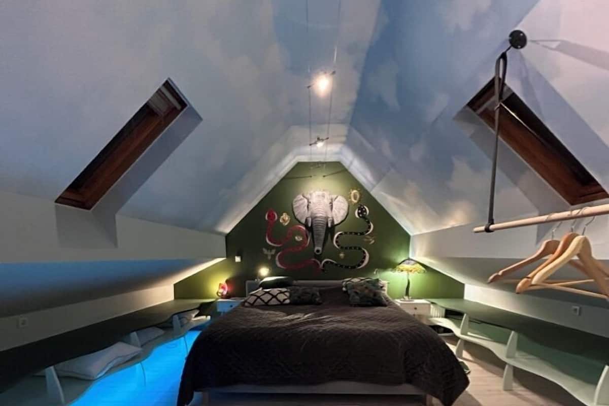 A bedroom with a sloped ceiling, a bed, a hanging light fixture, and a skylight.