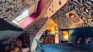 A bedroom with a sloped ceiling, a bed with a blue quilt, a chair, a desk, and a small window. - Wonderland21 (Saint-Germain-sur-Morin)