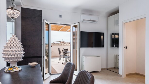 Een moderne woonkamer met een donkerhouten eettafel, twee gestoffeerde stoelen, een decoratieve witte vaas en een grote flatscreen televisie aan de muur.
