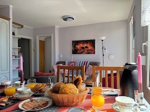 Ein Essbereich mit einem Tisch, gedeckt für das Frühstück, inklusive Brot, Gebäck und Orangensaft.