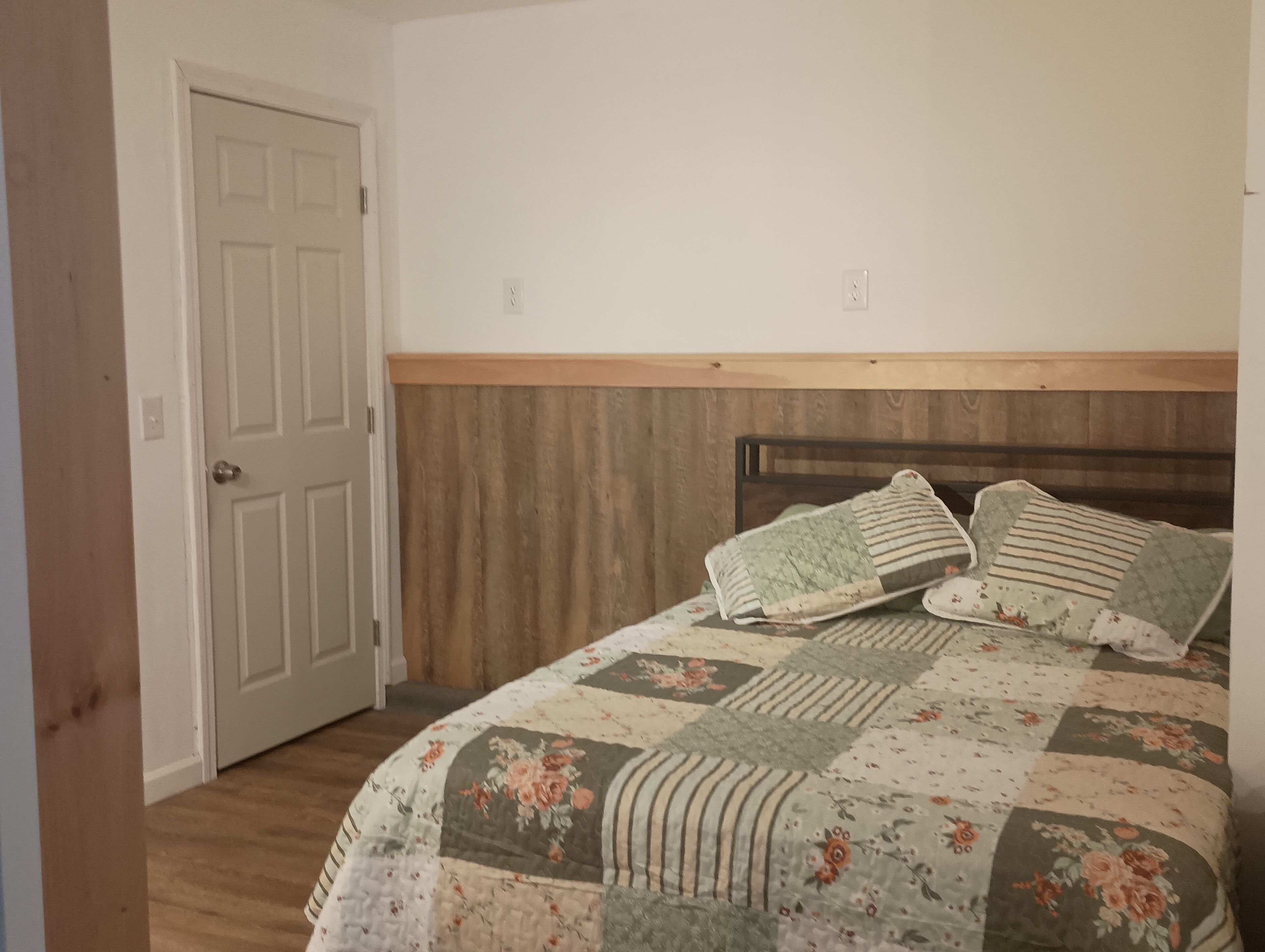 A bedroom with a wooden headboard, a floral quilt, and a closed door.