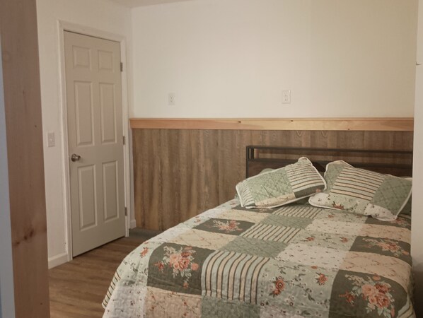 Ein Schlafzimmer mit einem hölzernen Kopfteil, einer Blumensteppdecke und einer geschlossenen Tür.