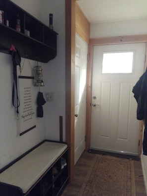 A hallway with a white door, a small window, a shelf with items, and a bench.