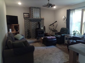 A living room with a fireplace, a television, a ceiling fan, and a window with curtains.
