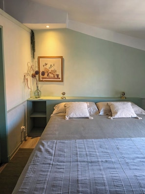 Ein Schlafzimmer mit einem Bett, Kissen, einem Nachttisch, einem Wandbild und einer Vase mit Trockenpflanzen.