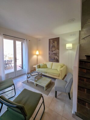 A living room with a sofa, a coffee table, and two chairs. There is a painting on the wall and a lamp on a side table. - Maison Charlotte - 4★ House with a courtyard, bicycles, 2 km from the beaches (Sainte-Marie-la-Mer)