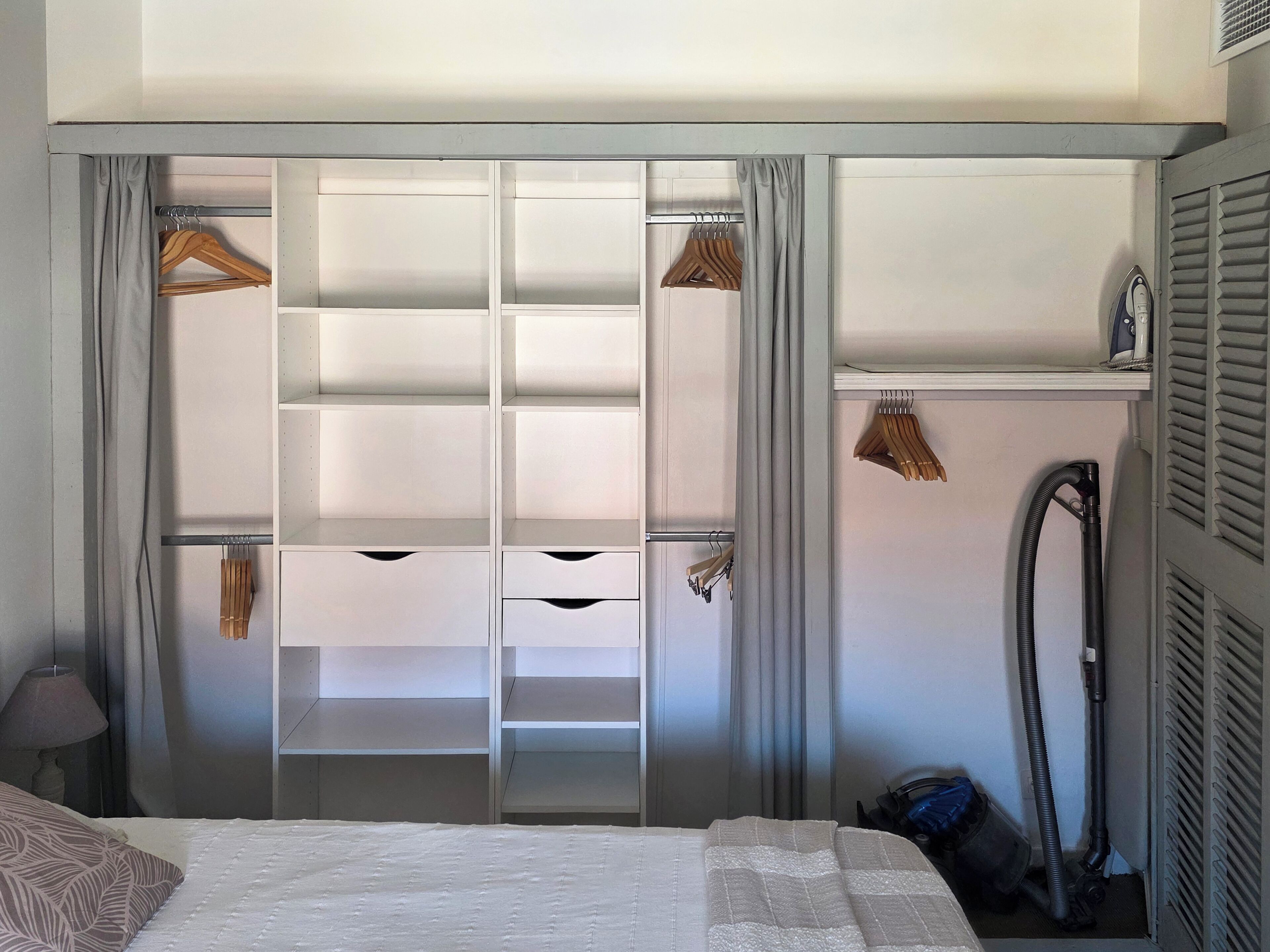 A bedroom with a bed, a wardrobe with multiple shelves, and a vacuum cleaner.