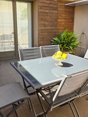 A glass-top table with a bowl of fruit and a potted plant, surrounded by mesh chairs. - Maison Charlotte - 4★ House with a courtyard, bicycles, 2 km from the beaches (Sainte-Marie-la-Mer)