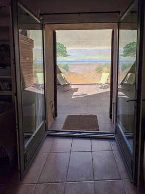 Eine Glastür führt zu einer Terrasse mit zwei Liegestühlen und Blick auf einen Strand.