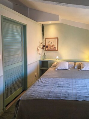 Ein Hotelzimmer mit einem Bett, einem Nachttisch, einem Wandbild und einem Fenster mit Jalousien.