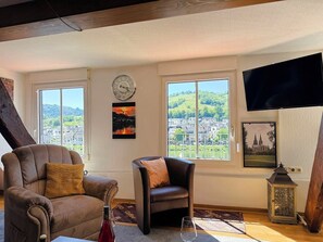 A room with a large window, a clock, a television, and a chair.