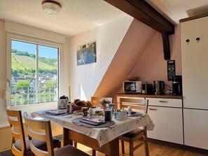 Een eethoek met een tafel voor twee personen, uitzicht op het platteland, en een keuken met een koelkast en magnetron.