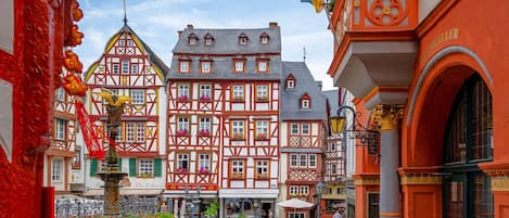 Ein Kopfsteinpflasterplatz mit traditionellen Fachwerkhäusern, einem Brunnen und Außenbereich-Sitzgelegenheiten.