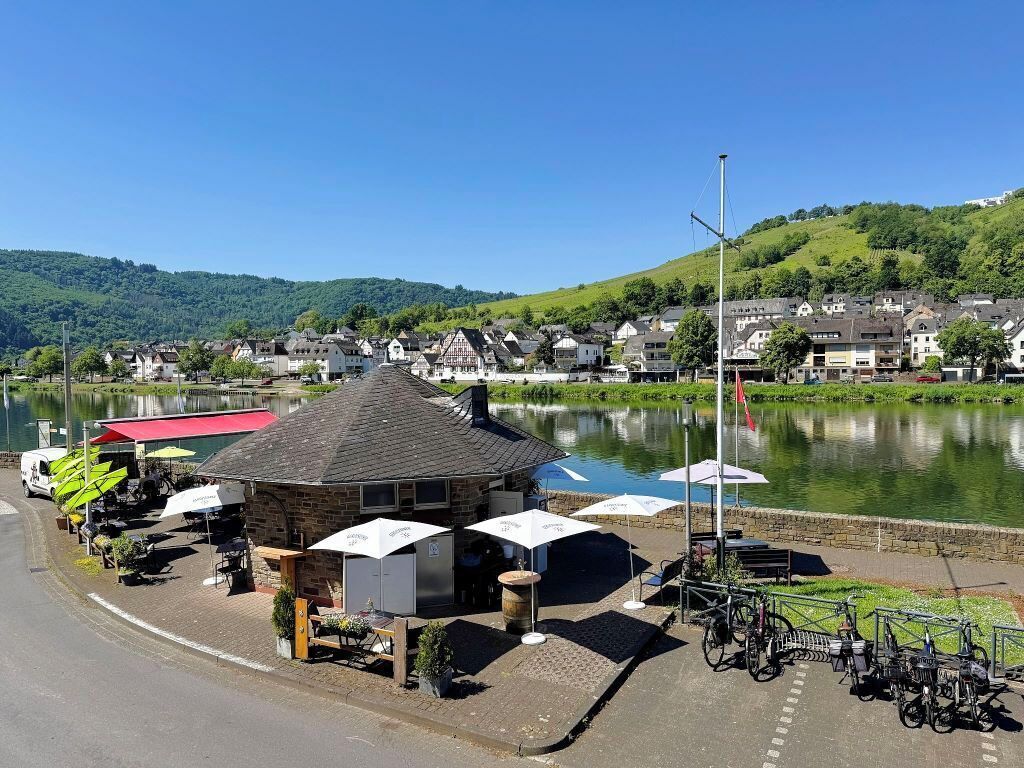 Un café junto al lago con terraza, bicicletas y un edificio de piedra.
