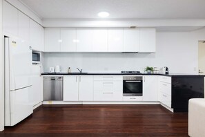 A modern kitchen with white cabinets, stainless steel appliances, and a wooden floor.