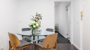 A modern dining area with a glass table, wooden chairs, and a vase of flowers. - Modern Comfort 2BR  Pool, Gym & Prime Valley Location (Fortitude Valley)