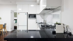 A modern kitchen with white cabinets, a black countertop, a microwave, and a coffee machine. - Modern Comfort 2BR  Pool, Gym & Prime Valley Location (Fortitude Valley)