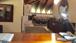 Ein gemütliches Dachzimmer mit Holzbalkendecke, einem Schreibtisch mit Lampe, einer Couch und einem Spiegel.