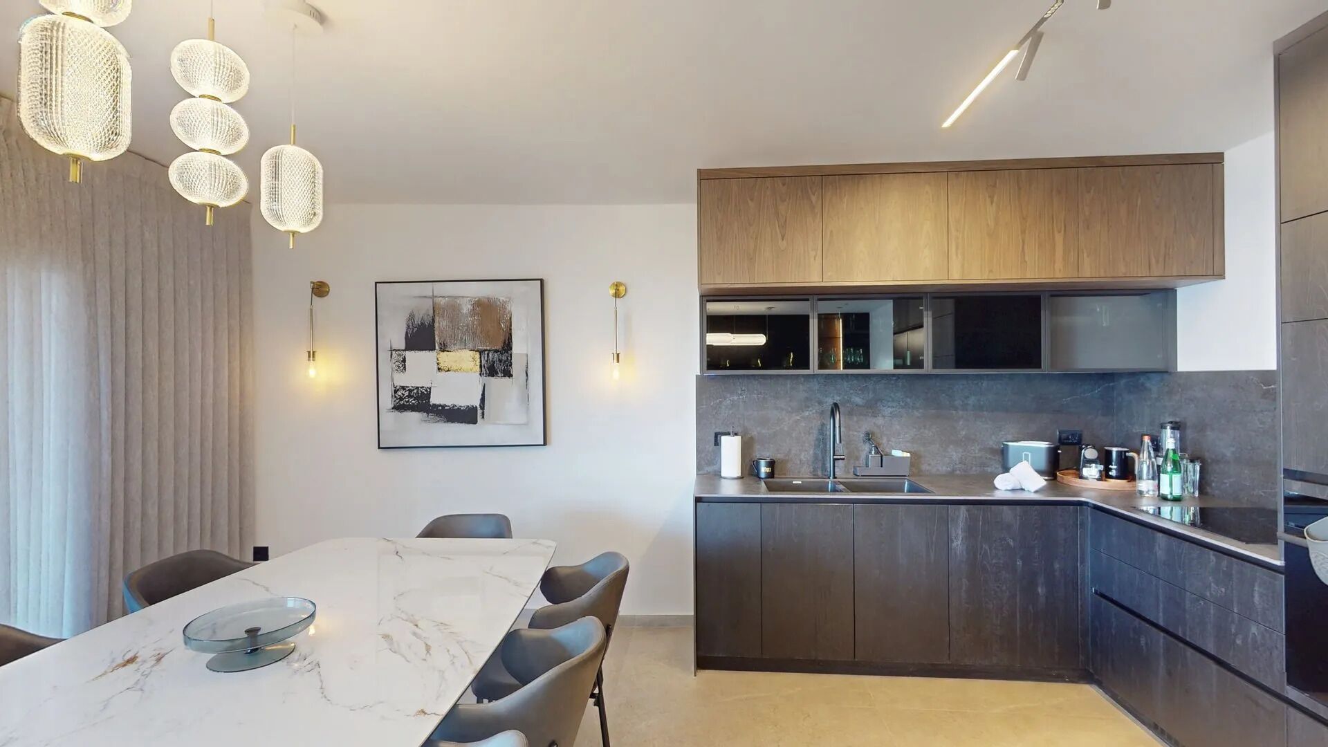 A modern kitchen with dark wood cabinets, a marble countertop, and pendant lighting.