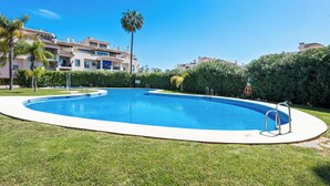 A swimming pool surrounded by well-maintained grass and palm trees, with a building in the background. - Lovely 2-bed 10 Mins Walk From Puerto Banus (Marbella)