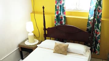 Una cama con cabecera de madera, una mesita de noche con lámpara y una ventana con cortinas florales.