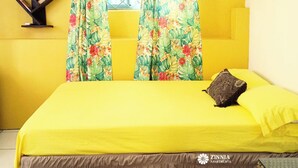Ein Zimmer mit einem gelben Bett, floralen Vorhängen, einer Wand-Klimaanlage und einem schwarzen Bücherregal.