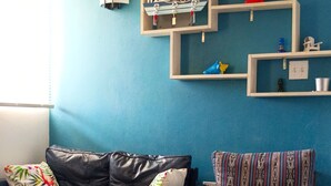 Un salon avec un mur bleu, un canapé en cuir noir, un fauteuil à motifs, une table basse en bois et un panneau « BIENVENUE » accroché au mur.