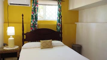 Quarto com cama, luminária de cabeceira, ar condicionado e janela com cortinas.