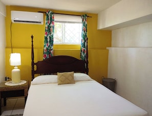 Un dormitorio con cama, lámpara de noche, equipo de aire acondicionado y ventana con cortinas.