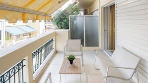 Ein Balkon mit gelbem, gemustertem Himmel, weißen Möbeln und Blick auf die Stadt.